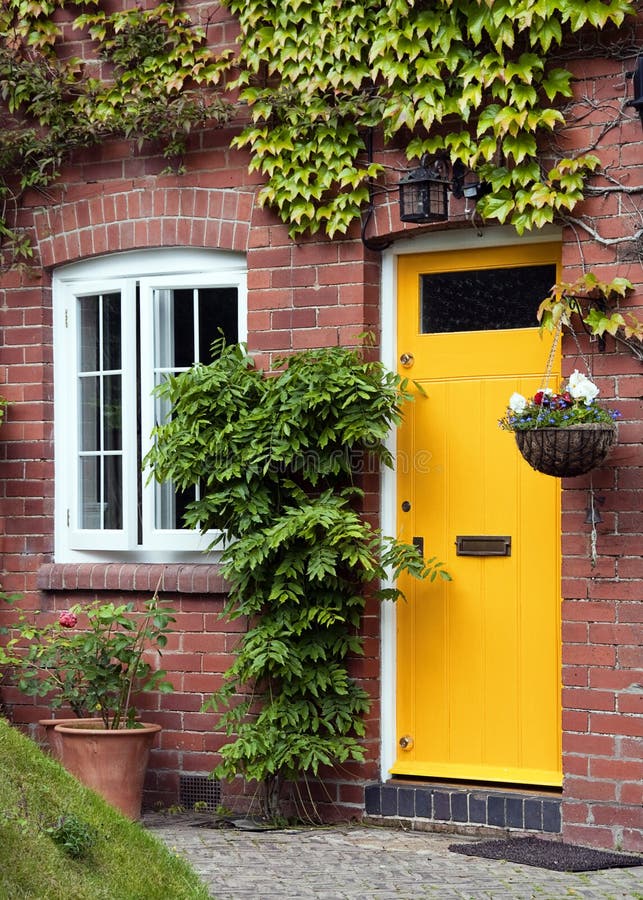 Front door. Yellow front door entrance and old style window of a red brick house or a cottage with hanging flower basket and green ivy royalty free stock photography